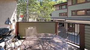A patio with a round metal table and chairs, a grill, and a wooden deck. - Spacious Townhome on Shuttle Route, Just Minutes to Vail Resort! (Vail)