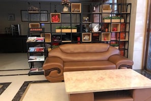A brown leather sofa, a small table, and a bookshelf with various items. - Wenzhou Jinfeng Business Hotel (Yongjia)