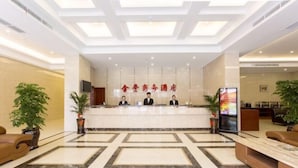 Zona de recepción de un hotel con piso de mármol, mostrador de recepción y dos recepcionistas.