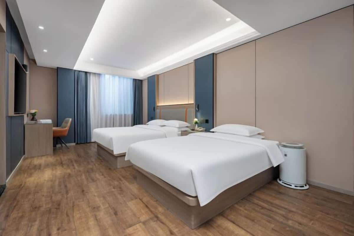 Een hotelkamer met drie bedden, een bureau, een stoel en een prullenbak.