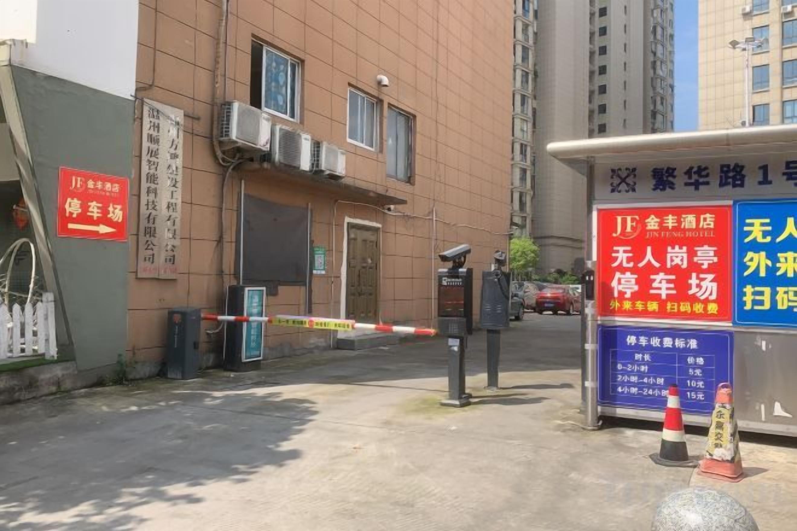 Un estacionamiento cerrado con acceso a un edificio, una caseta de seguridad y un letrero con texto.