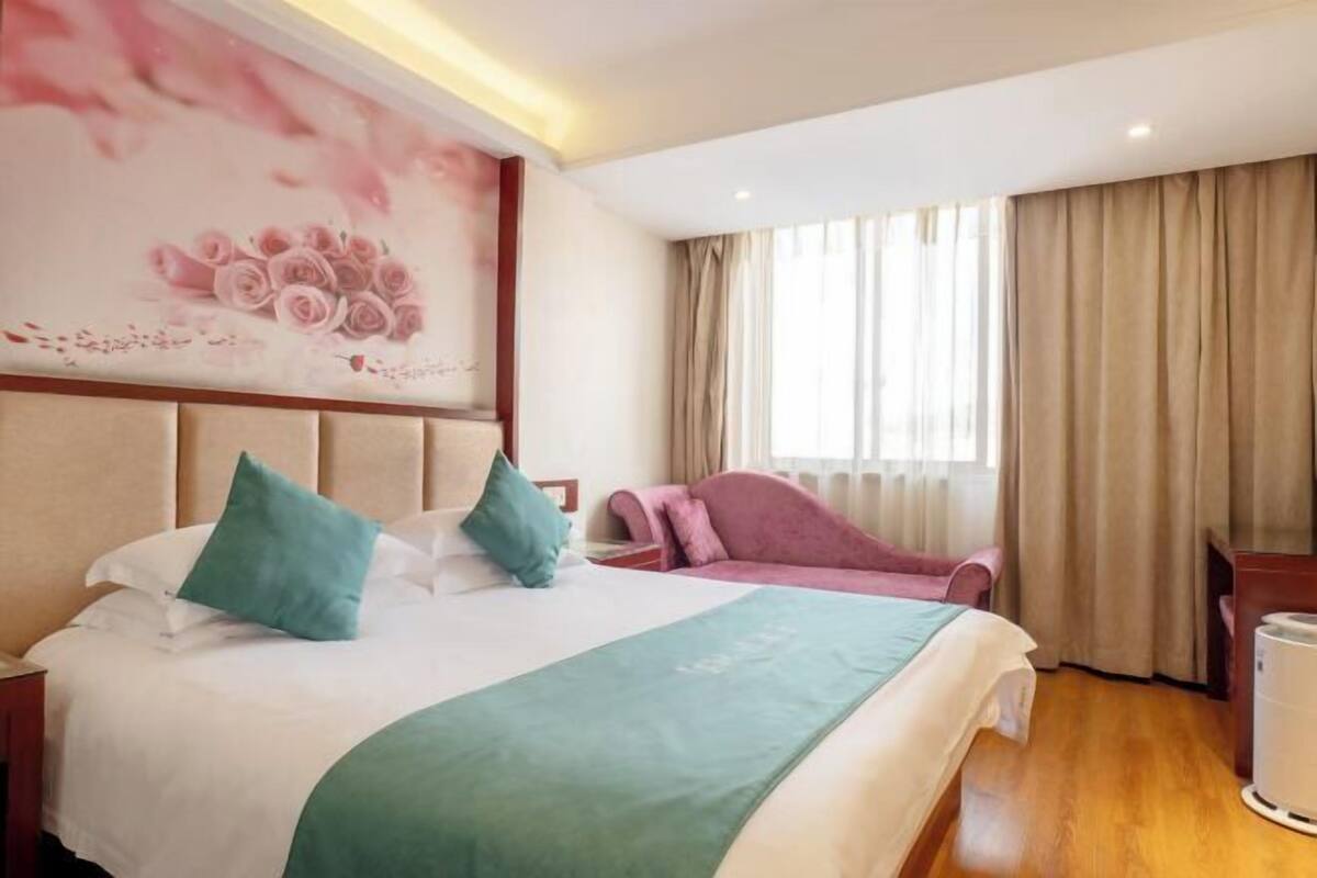 Een hotelkamer met een bed, een bureau, een stoel en een groot raam met gordijnen.