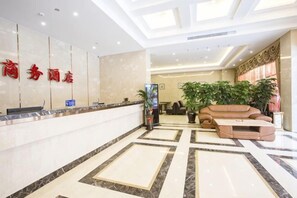 A hotel lobby with a reception desk, a seating area with a sofa and a coffee table, and a large potted plant. - Wenzhou Jinfeng Business Hotel (Yongjia)