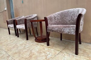 A row of three sofas with wooden legs and a round table in between, against a plain wall.