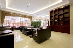 Eine Hotelhalle mit Sitzbereichen, einer Rezeption und einem großen Fenster mit Vorhängen.