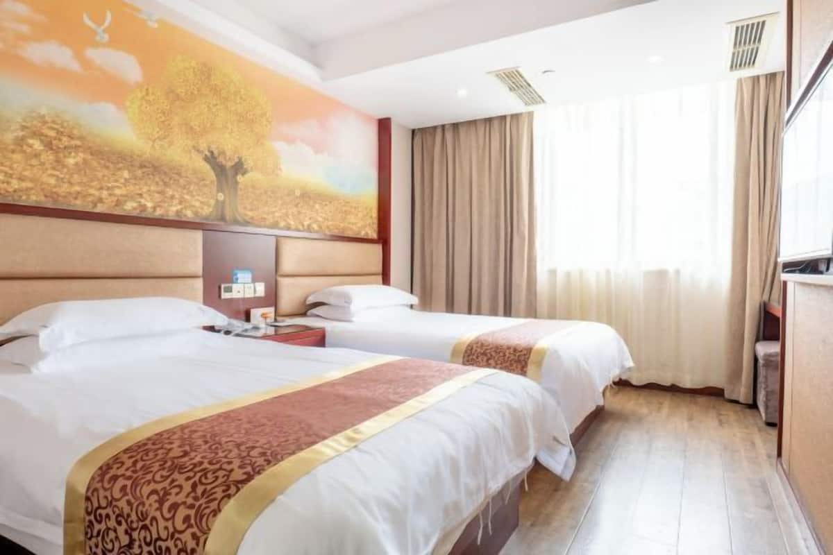Een hotelkamer met twee bedden, een groot schilderij van een boom, een bureau en een raam met gordijnen.