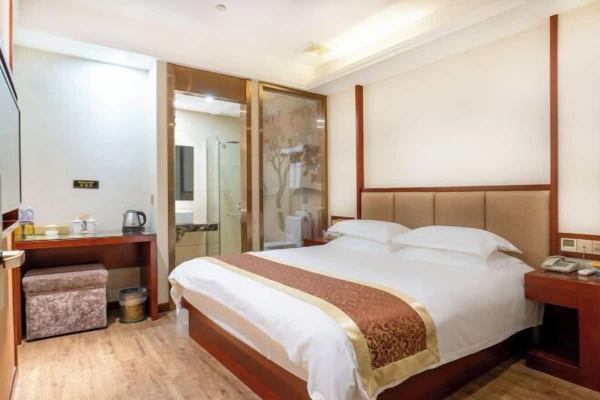 Een hotelkamer met een bed, een bureau, een stoel, een klein tafeltje en een prullenbak.