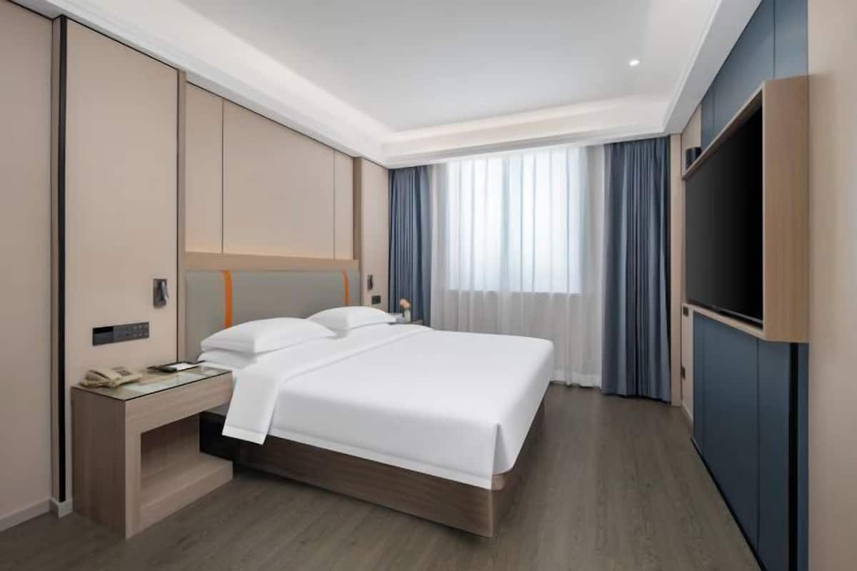 Een moderne hotelkamer met een bed, nachtkastje, televisie en gordijnen.