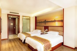 Habitación de hotel con dos camas, un ventanal con vistas al atardecer, una puerta y una mesita con lámpara.