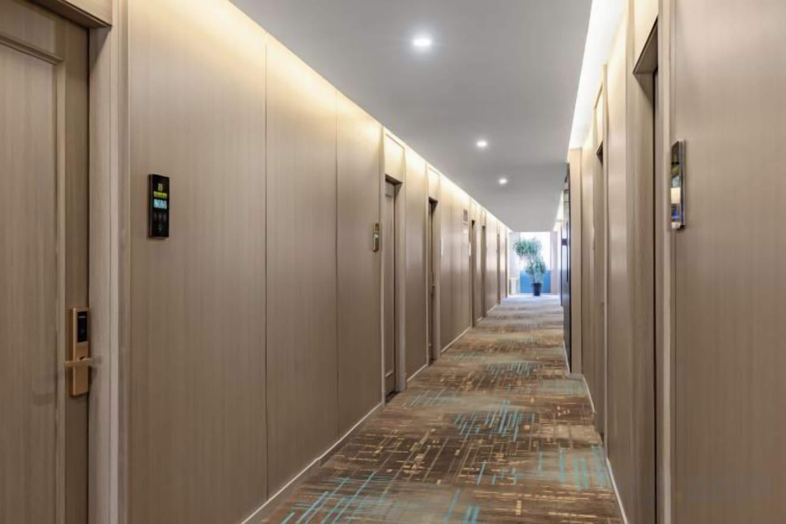 Un pasillo de hotel con puertas a ambos lados, una alfombra estampada e iluminación empotrada en el techo.