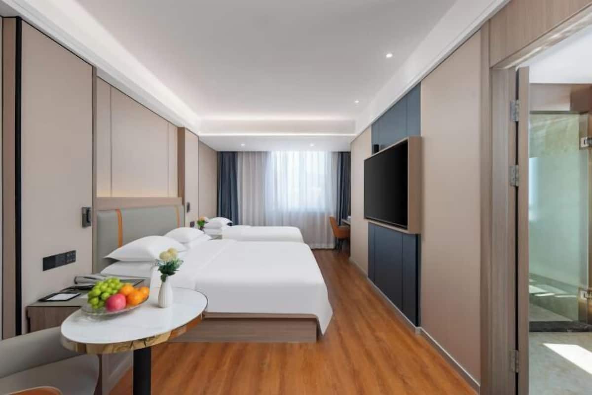 Een hotelkamer met twee bedden, een televisie, een klein tafeltje met fruit en een raam met gordijnen.