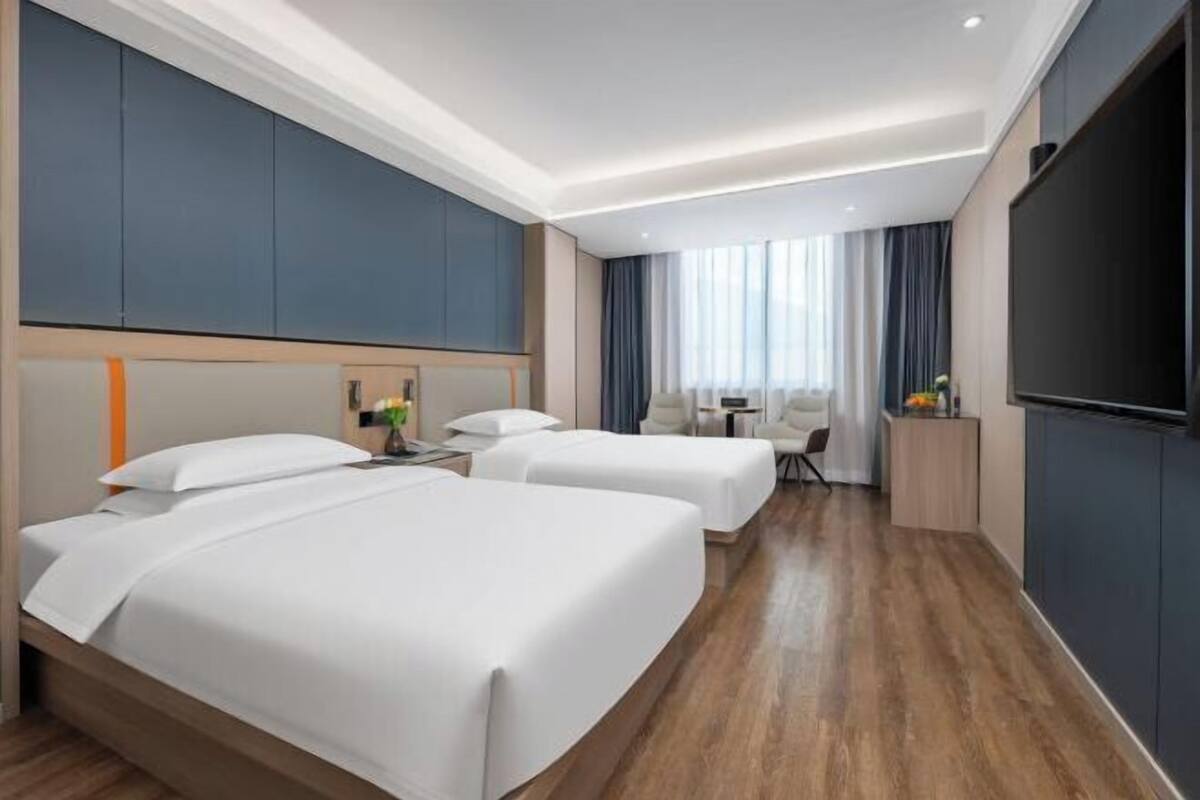 Een hotelkamer met twee bedden, een bureau, een stoel, een televisie en een groot raam met gordijnen.