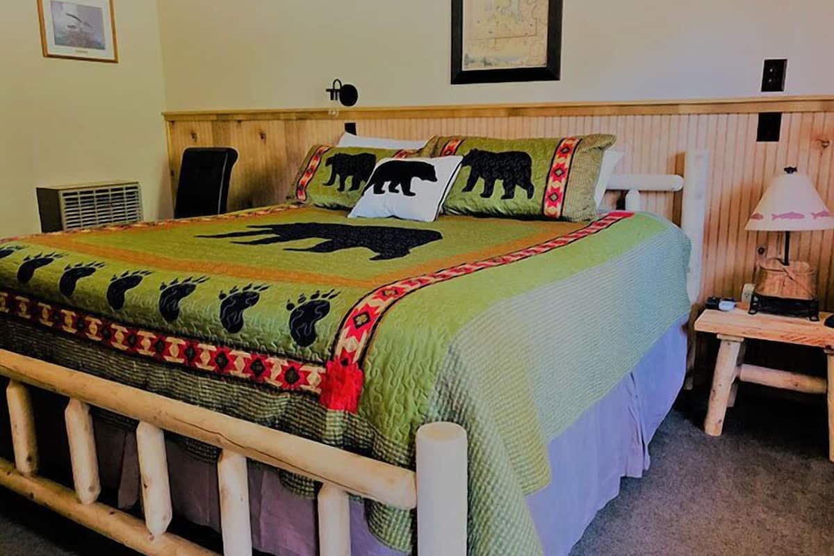 A bed with a green blanket featuring animal prints, a wooden headboard, and a small bedside table with a lamp.
