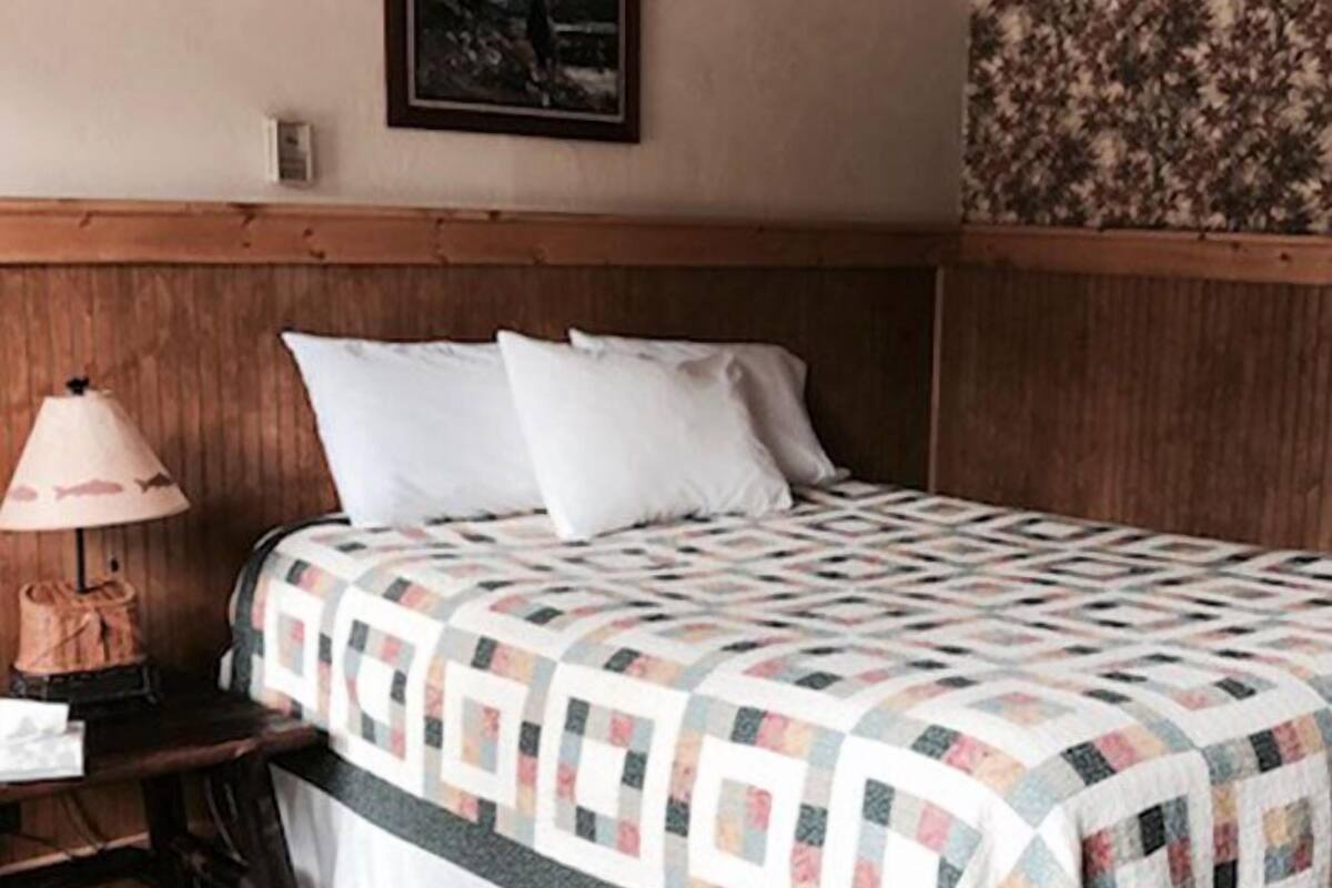 A hotel room with a wooden headboard, a quilted bedspread, a nightstand with a lamp, and a framed picture on the wall.