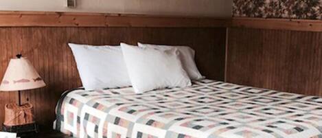 A hotel room with a wooden headboard, a quilted bedspread, a nightstand with a lamp, and a framed picture on the wall.
