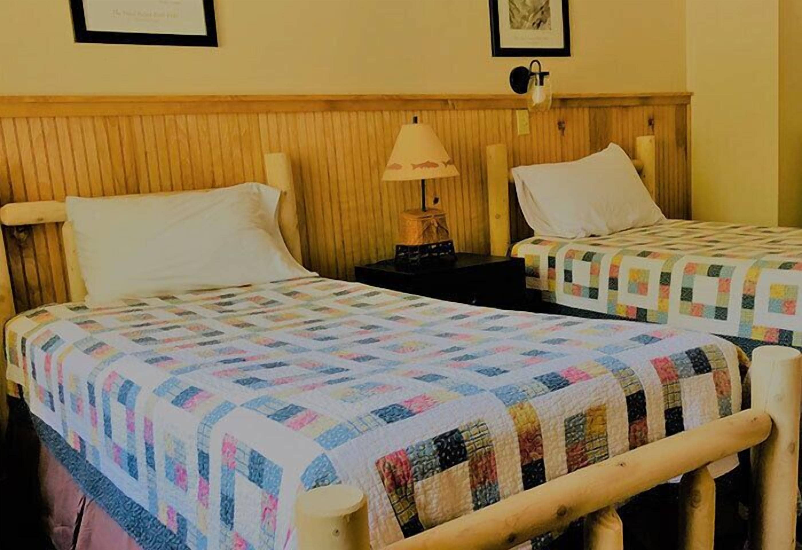 Two single beds with wooden headboards, a nightstand with a lamp, and a quilted bedspread.