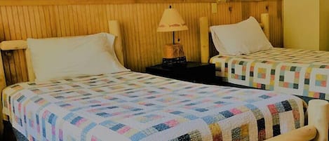Two single beds with wooden headboards, a nightstand with a lamp, and a quilted bedspread.