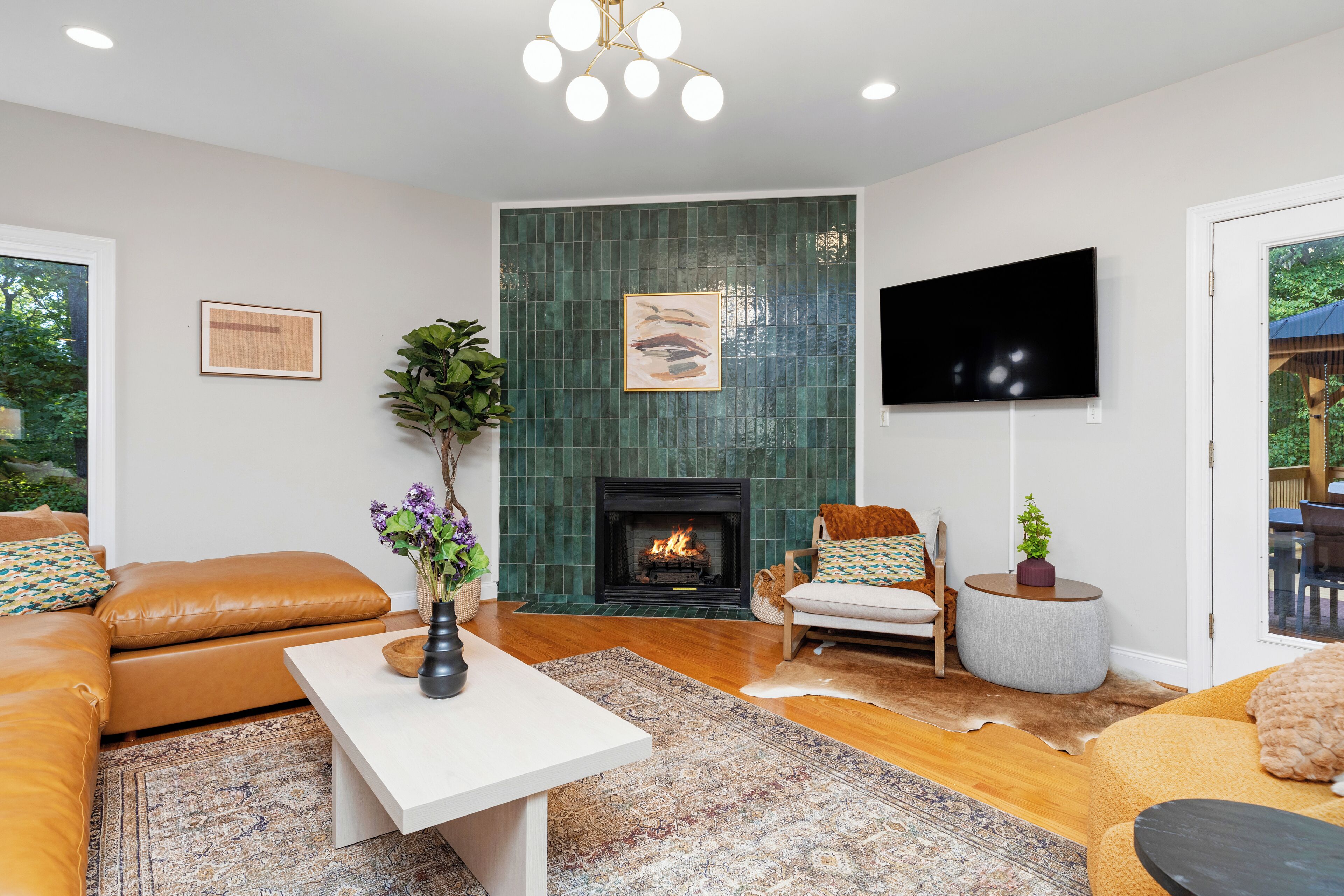 A living room with a fireplace, leather sofas, a flat-screen TV, and a large window.