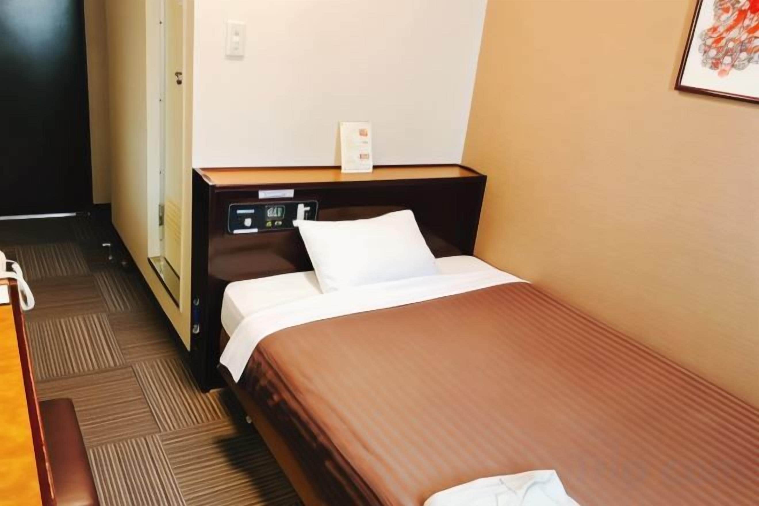 A hotel room with a single bed, a bedside table, a nightstand, and a wall-mounted telephone.