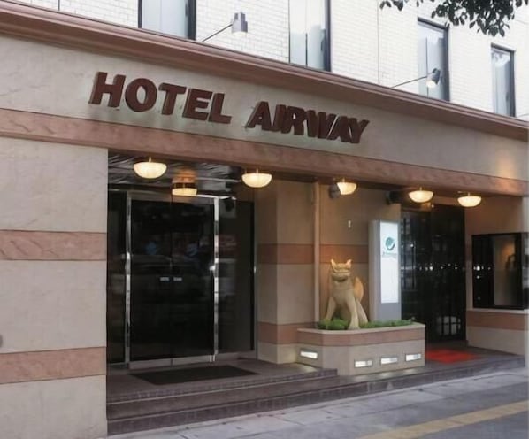 A hotel entrance with a sign reading 'HOTEL AIRWAY,' a glass door, and a small statue of a dog. - Hotel Airway (Naha)