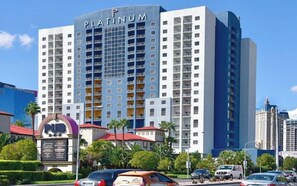 Un hotel de gran altura con un letrero llamativo que dice "PLATINUM", múltiples balcones y una zona bien cuidada con palmeras y coches estacionados.