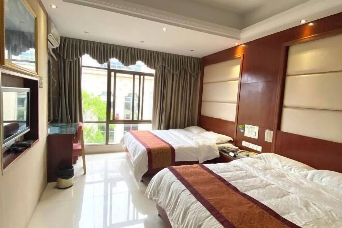 Une chambre d’hôtel avec deux lits, une télévision, un bureau et une grande fenêtre avec des rideaux.