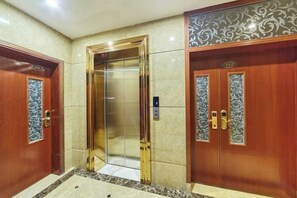 A hotel elevator with a metallic interior, flanked by wooden doors with intricate designs.