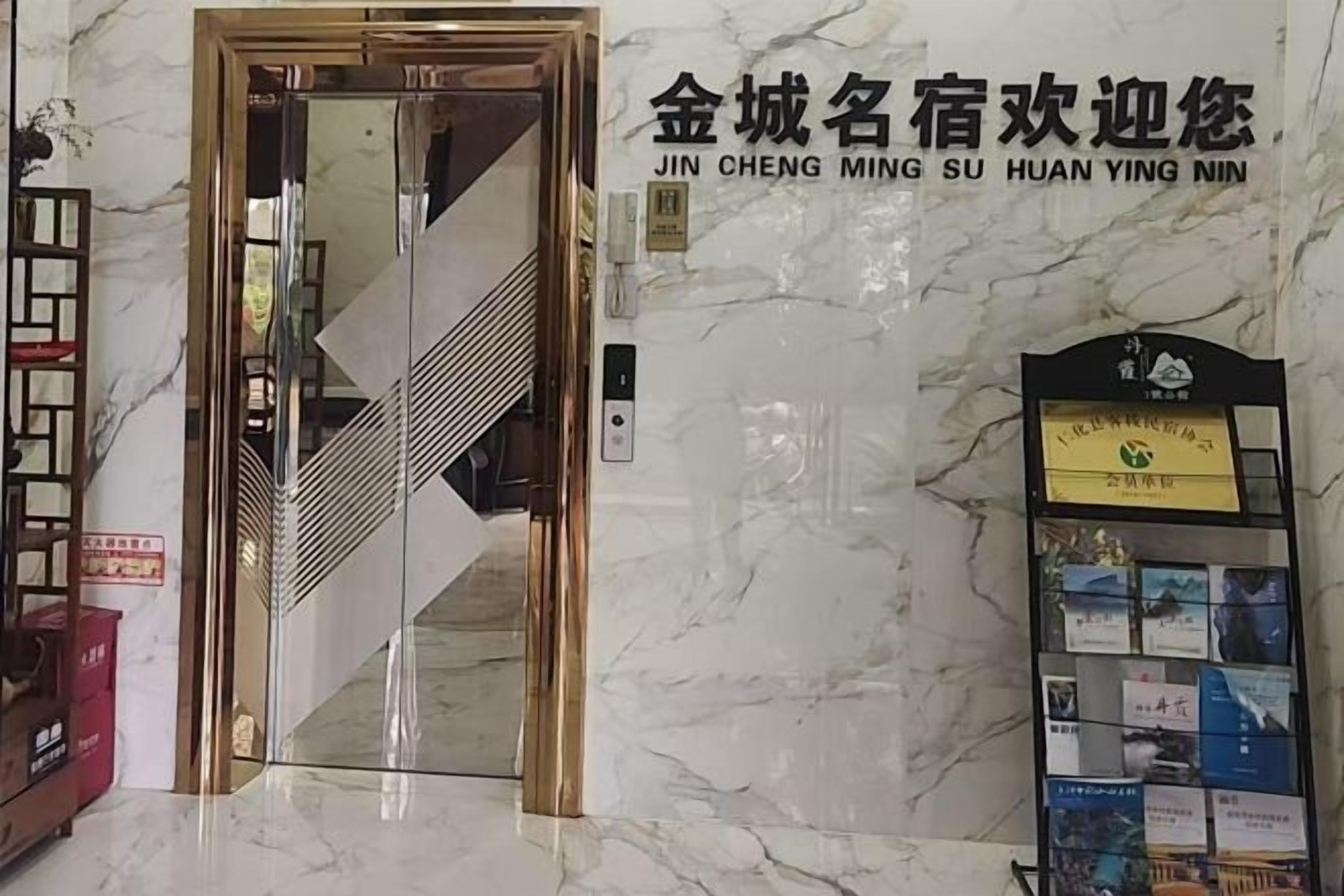 A hotel entrance with a marble wall, a reception desk, and a staircase.