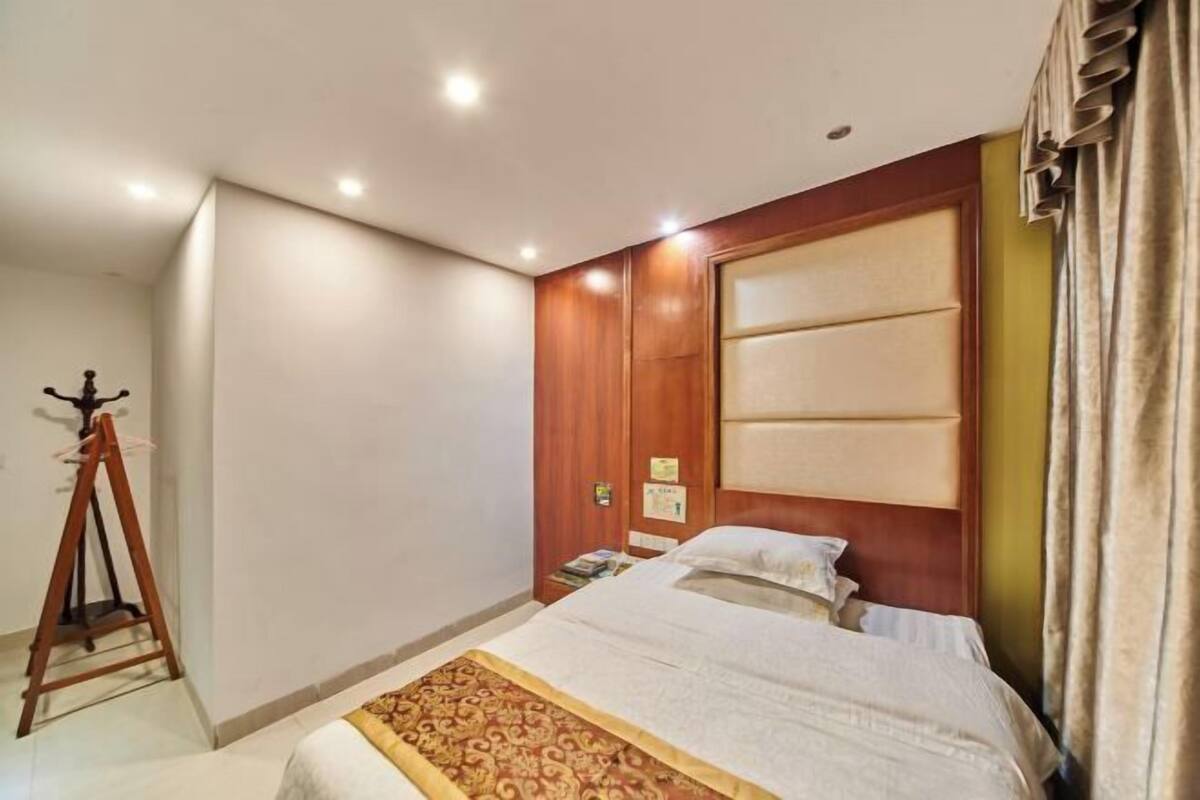 Une chambre d’hôtel avec un lit, une armoire en bois, une petite table avec une lampe et un rideau.