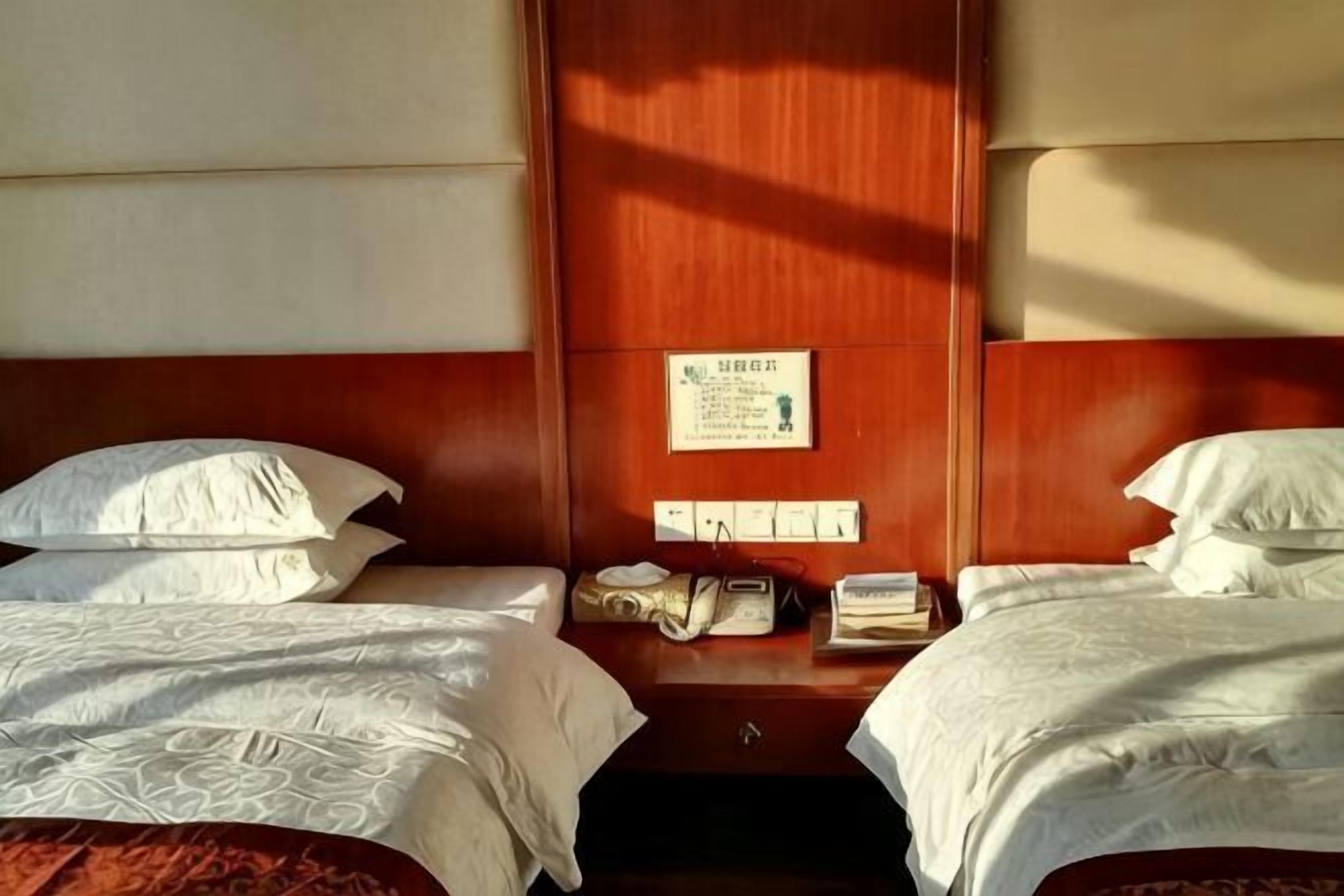 Une chambre d’hôtel avec deux lits, une tête de lit en bois, une table de chevet avec un téléphone et un panneau fixé au mur.