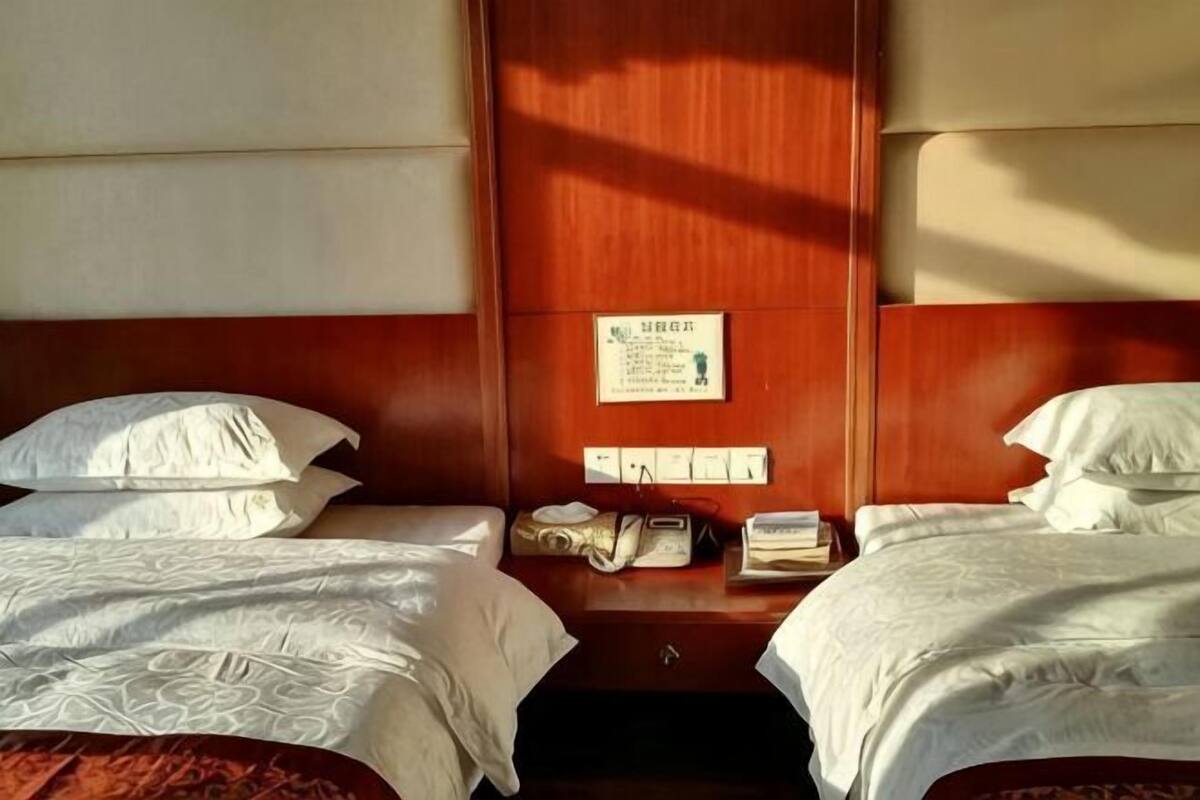 Une chambre d’hôtel avec deux lits, une tête de lit en bois, une table de chevet avec un téléphone et un panneau fixé au mur.