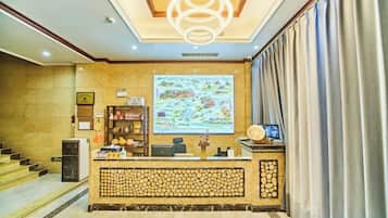 A hotel reception area with a reception desk, a large map on the wall, a staircase, and a decorative wall panel.