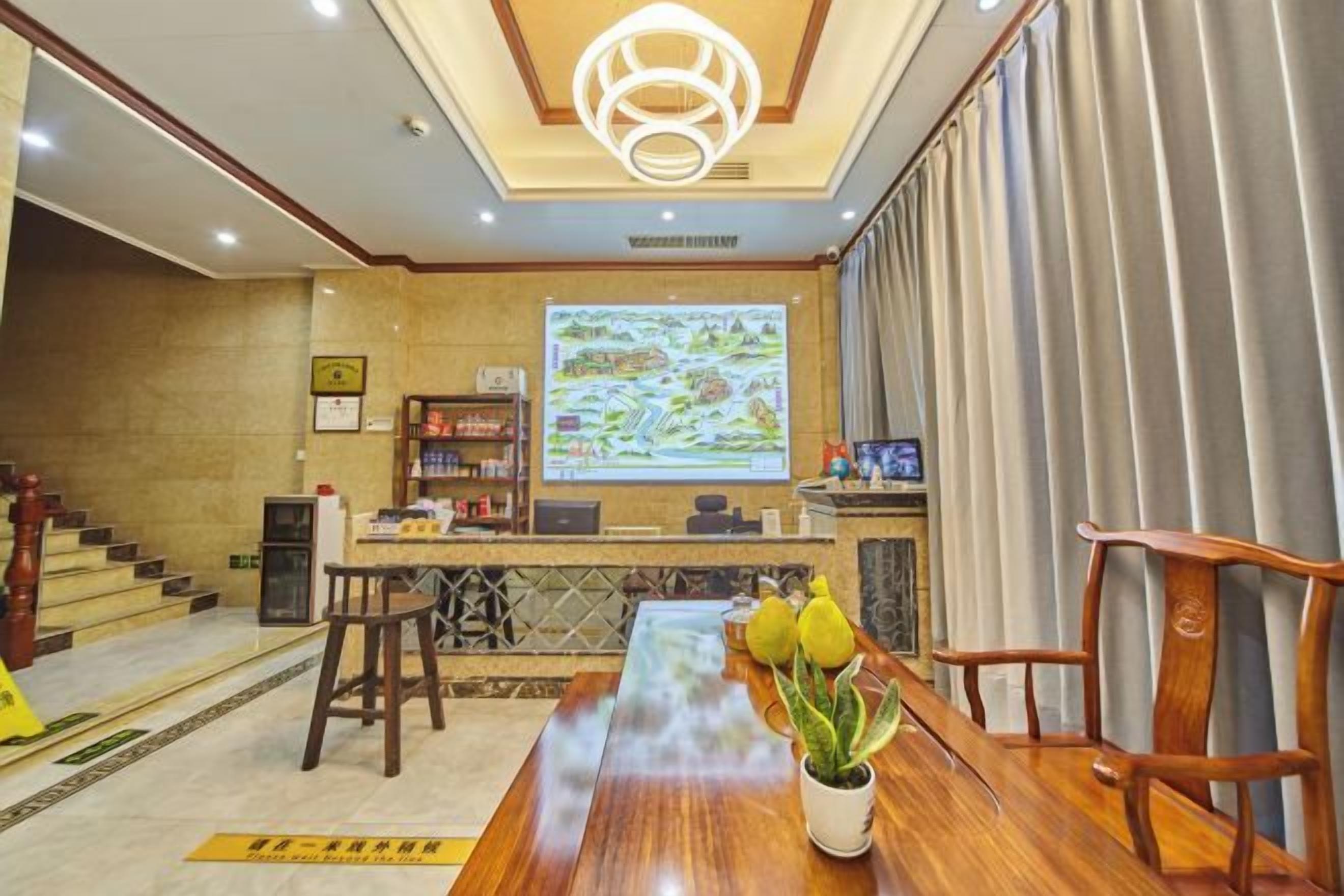 A hotel lobby with a reception desk, a large screen displaying a map, a wooden reception desk, and a reception area with a staircase.