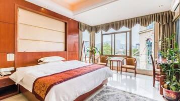 A hotel room with a large bed, a desk, a chair, and a view of the city.