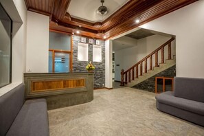 Un espace d’accueil avec un comptoir de réception en bois, un mur en pierre et un escalier menant aux étages supérieurs.