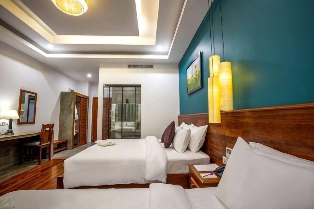 Habitación de hotel con dos camas, un escritorio y vistas al exterior.