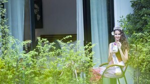 A person seated at a table with a drink, surrounded by greenery and a building with large windows. - The Tito Suite Residence (Siem Reap)