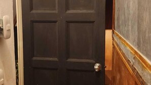 Uma porta preta com um aldabinha em formato de cabeça de cachorro, piso estampado e detalhes em madeira.