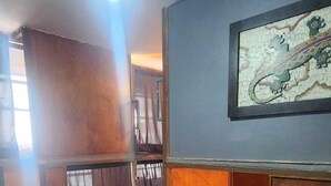 Um quarto com piso de madeira, uma cama com cobertor listrado, uma prateleira fixada na parede com um quadro emoldurado e um lustre no teto.