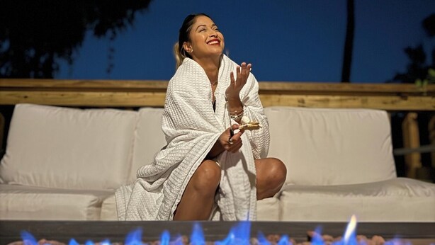 Una persona sentada en un sofá blanco al aire libre, con una chimenea exterior delante.