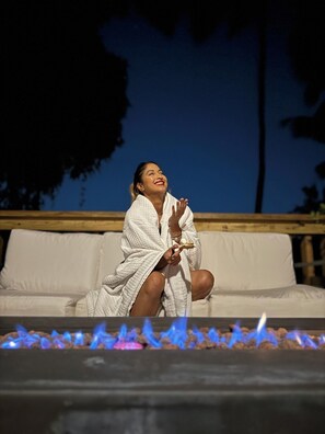 A person sitting on a white outdoor sofa with a fire feature in front. - The ONLY glamping site in the New Millennium Forest in San Juan, PR (San Juan)