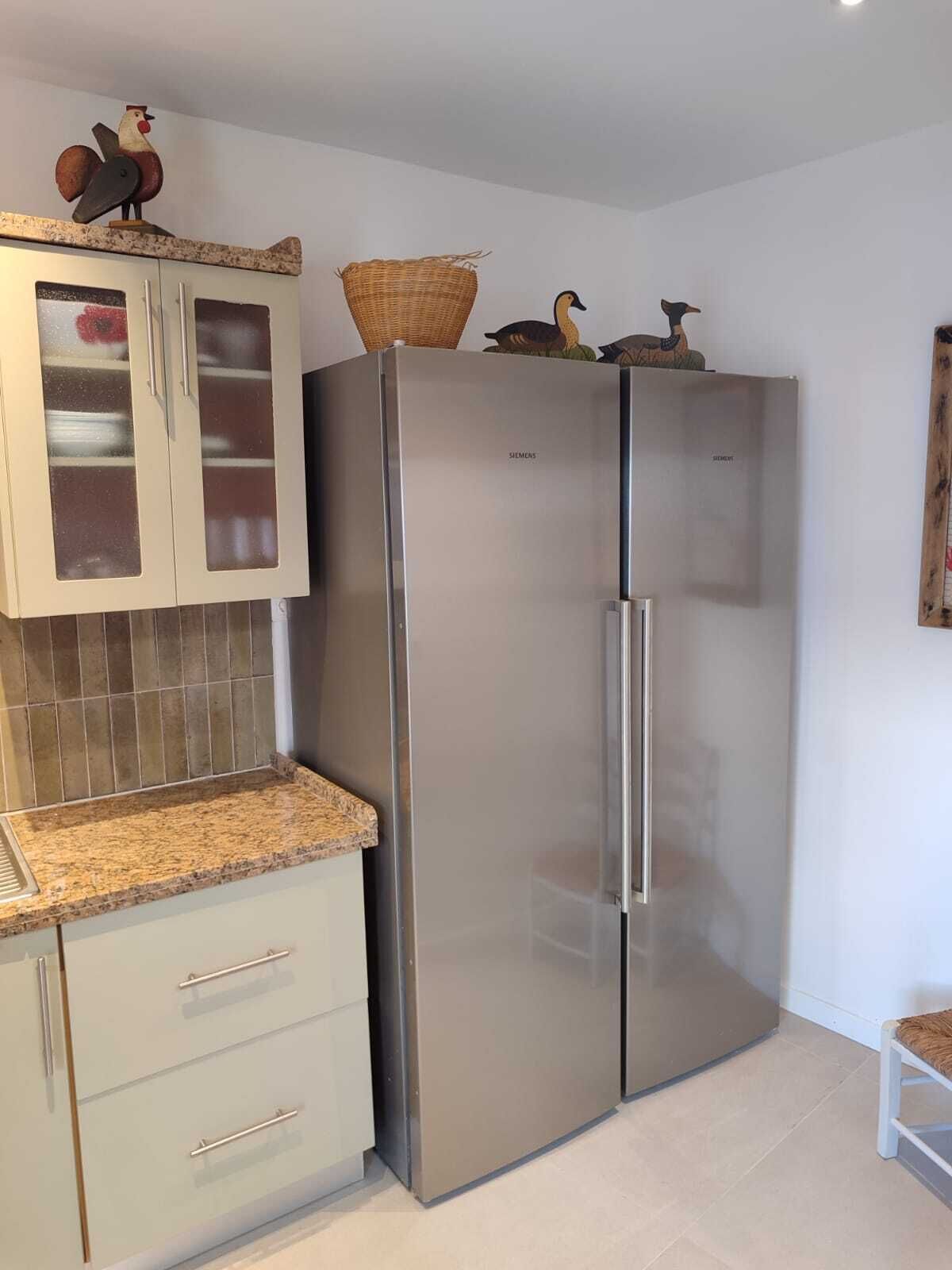A kitchen with a stainless steel refrigerator, a wooden cabinet with glass doors, and a granite countertop.