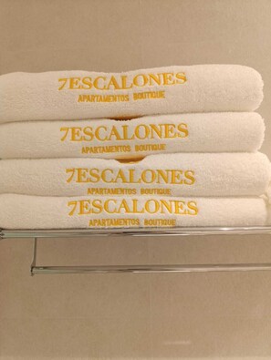 Four folded white towels stacked on a glass shelf with embroidered text. - Mina25 by 7Escalones (Rota)