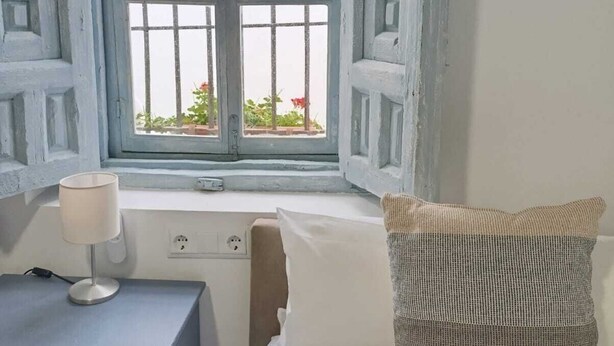 Une pièce avec un lit, un bureau doté d’une lampe et une fenêtre dont les volets sont ouverts.