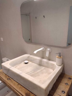 Une salle de bain avec un lavabo en marbre blanc, un meuble-lavabo en bois et un miroir au-dessus du lavabo.