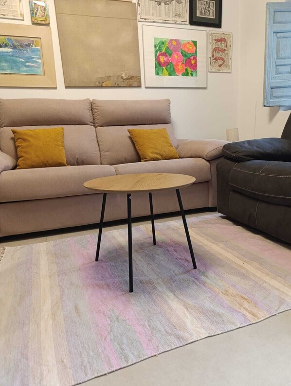 Un salon avec un canapé beige, une table basse ronde en bois et un tapis rayé multicolore.