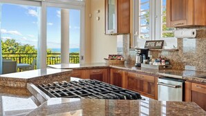 A kitchen with a coffee bar, granite countertops, wooden cabinets, and a view of the ocean.