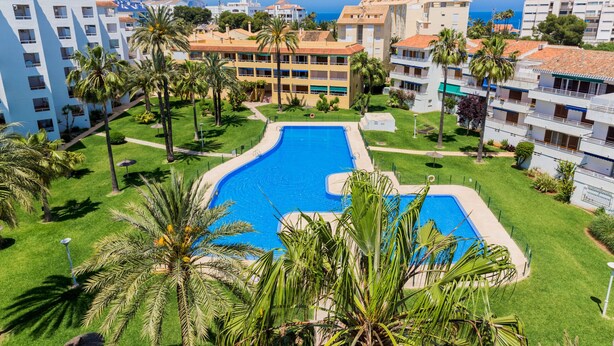 Un hotel con piscina central rodeada de palmeras y vistas al mar.