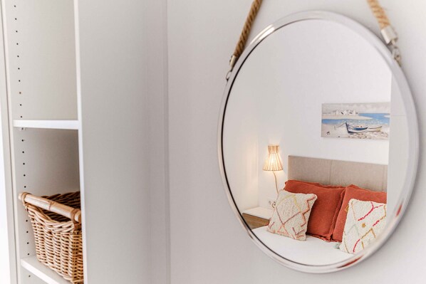 A round mirror reflecting a bed with a headboard, a lamp, and a painting on the wall.