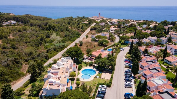 An aerial view of a coastal residential area with houses, a swimming pool, and a lighthouse in the distance. - Casa Mia by LovelyStay (Carvoeiro)